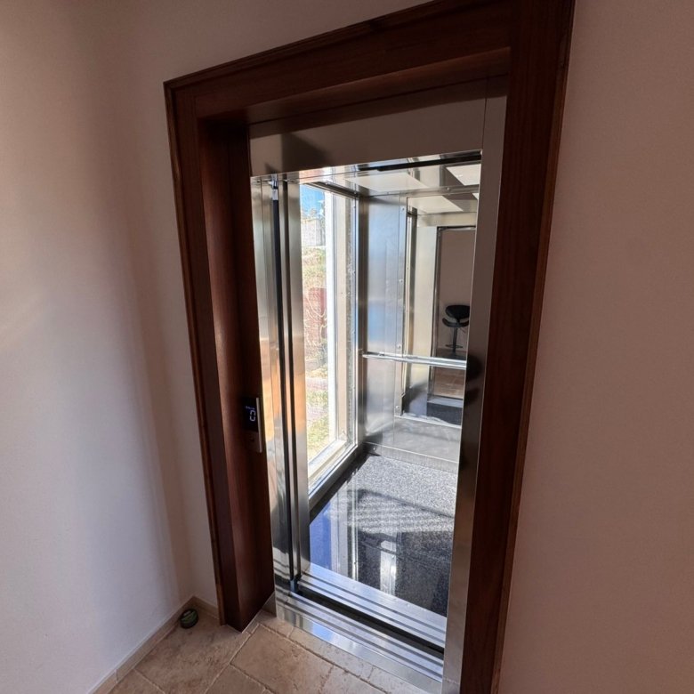 Luxurious elevator with glass walls, mirrored ceiling, and beige tiles&mdash;premium Ulcinj real estate by immorenta.me.