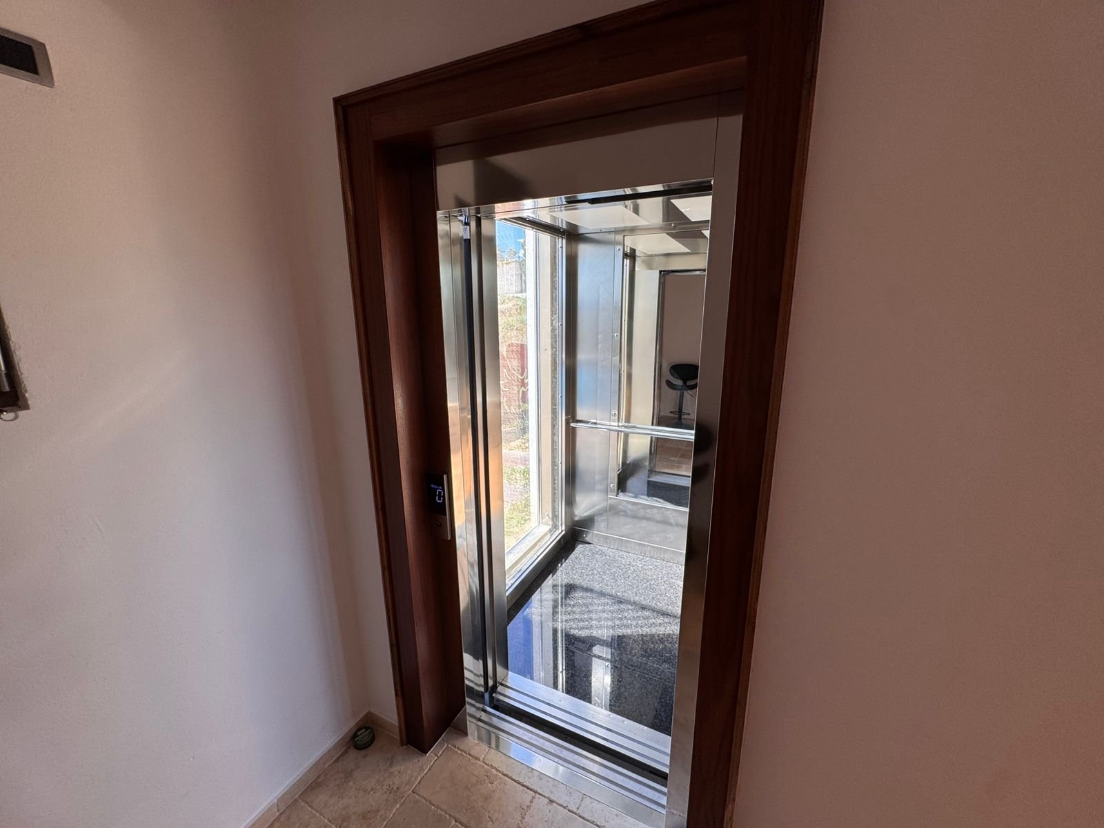 Luxurious elevator with glass walls, mirrored ceiling, and beige tiles&mdash;premium Ulcinj real estate by immorenta.me.
