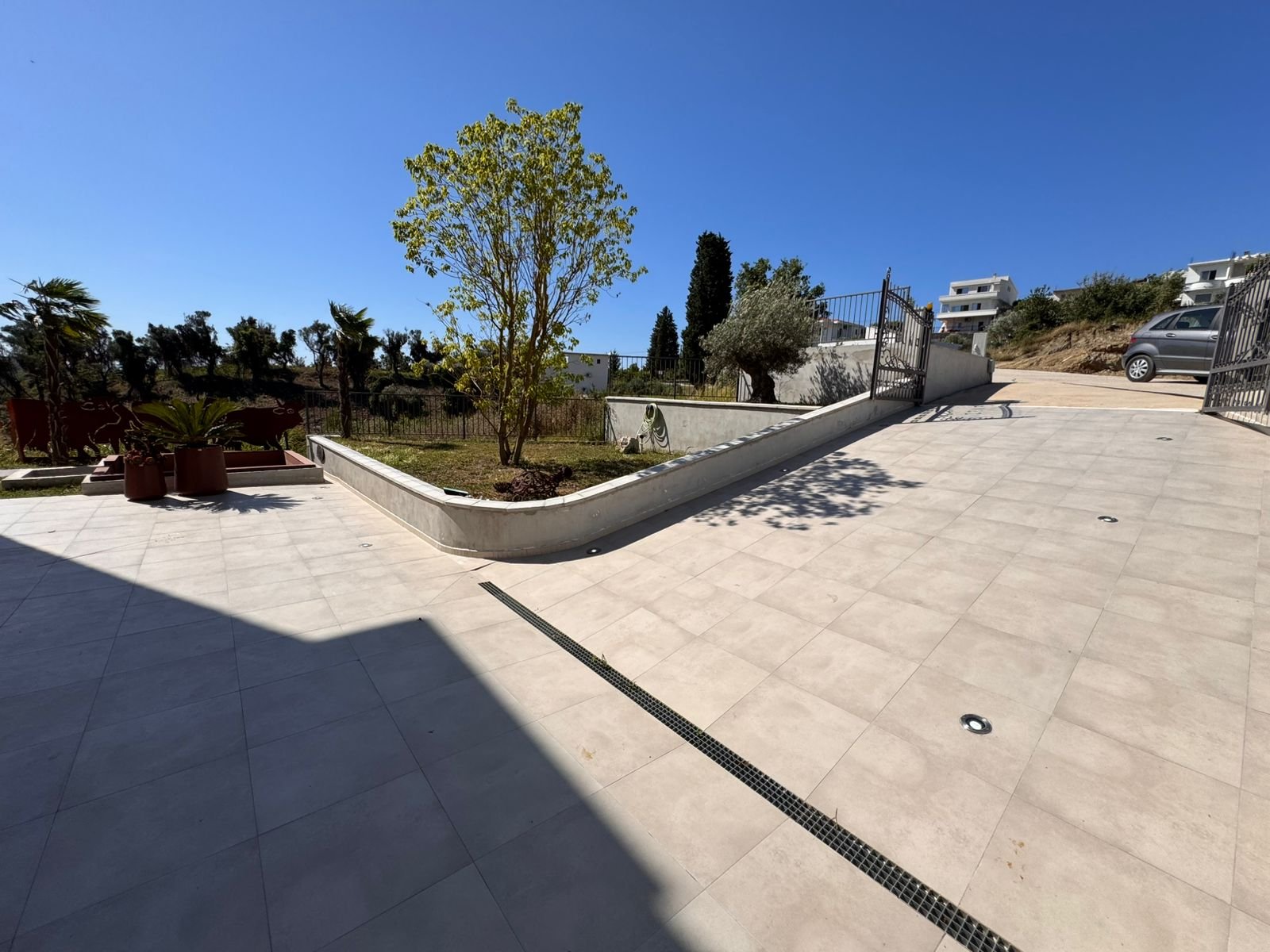 Modern paved terrace with elegant tiles, lush greenery, secure metal gate, and private parking&mdash;prime Ulcinj property on immorenta.me by ekosphere doo.