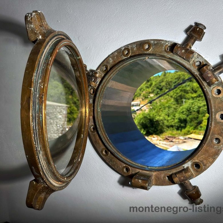 Open brass porthole on white wall reveals lush Ulcinj views&mdash;explore top Montenegro real estate at immorenta.me by ekosphere doo.