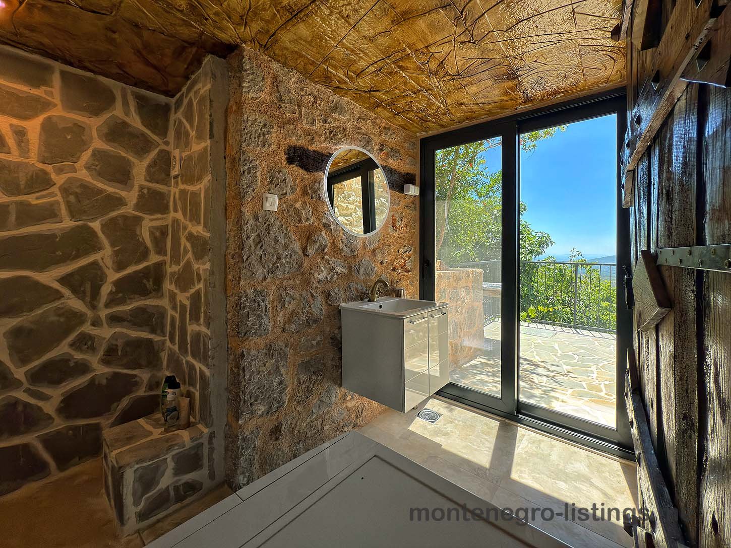 Discover an authentic Ulcinj property: rustic stone-wall bathroom, modern fixtures, patio access. Montenegro-listings.me by Ekosphere doo.