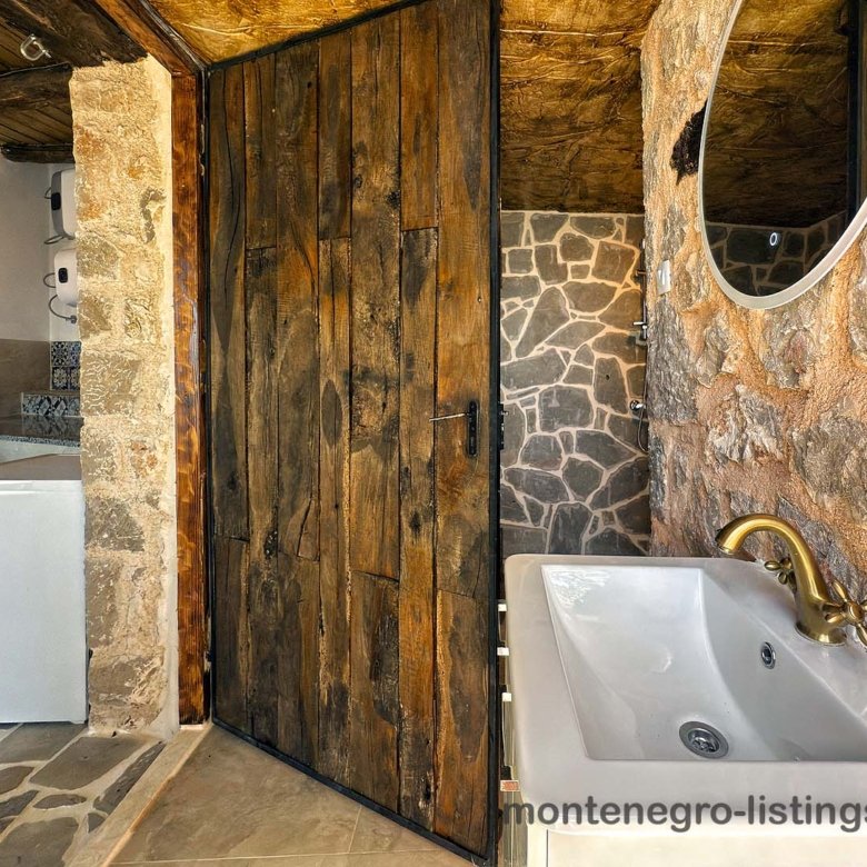 Elegant rustic bathroom with stone walls, wood door, chic brass accents; ideal Ulcinj investment via immorenta.me by ekosphere doo.