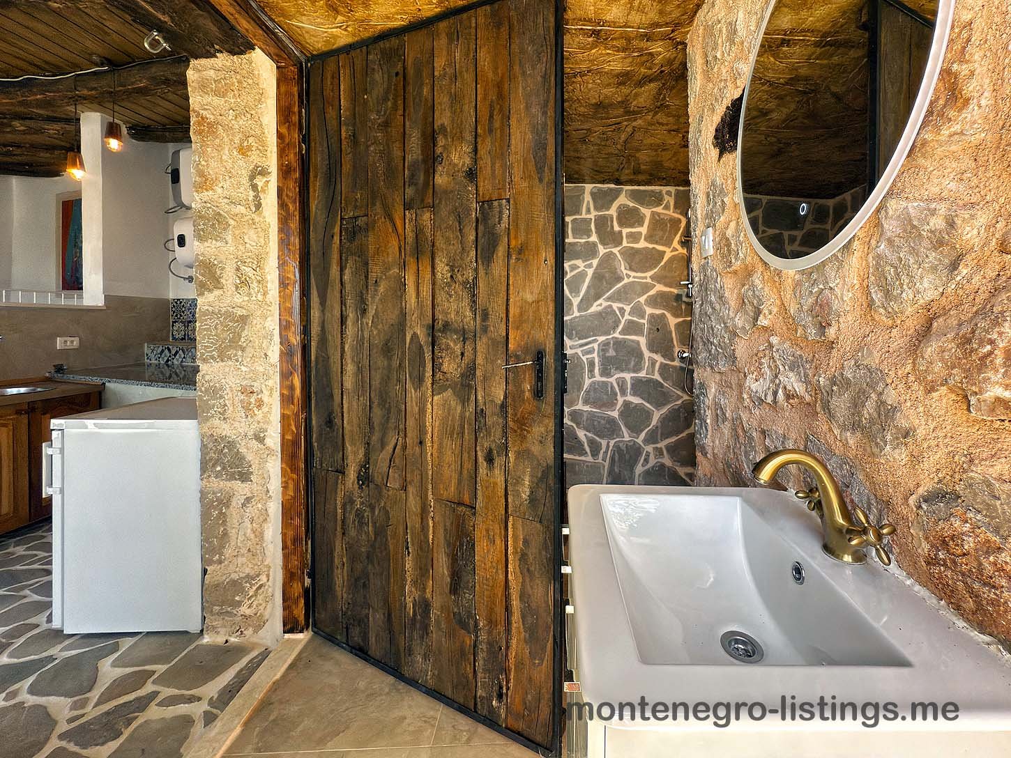 Elegant rustic bathroom with stone walls, wood door, chic brass accents; ideal Ulcinj investment via immorenta.me by ekosphere doo.