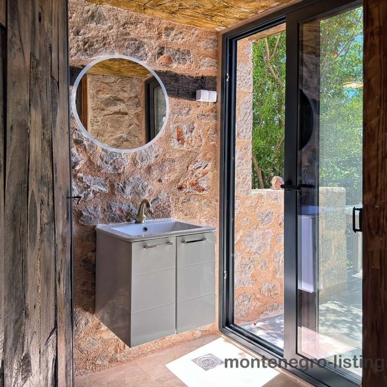 Luxury modern bathroom in Ulcinj, Montenegro: elegant gray vanity, stone walls, garden view. Invest with immorenta.me by Ekosphere.