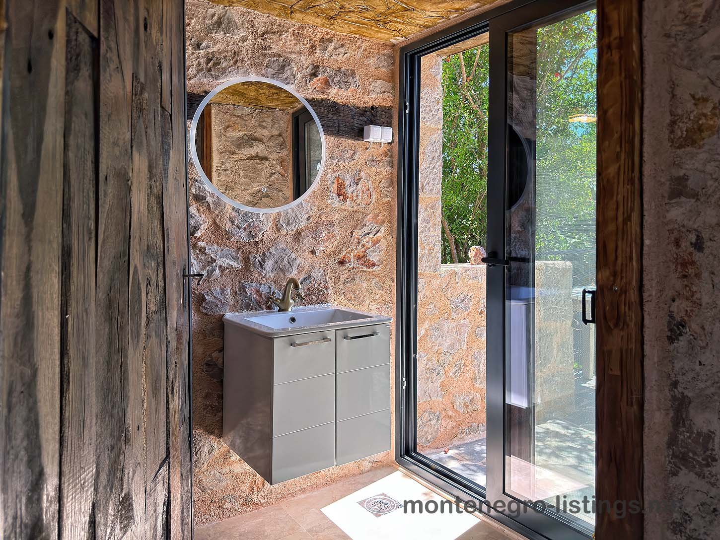 Luxury modern bathroom in Ulcinj, Montenegro: elegant gray vanity, stone walls, garden view. Invest with immorenta.me by Ekosphere.