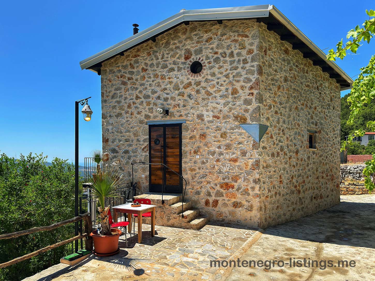 Charming stone house with black door, lush green surroundings, and stone terrace in Ulcinj, Montenegro. immorenta.me by ekosphere doo.