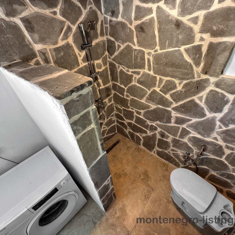 Modern bathroom in Ulcinj with stone tiles, open shower, washer, & toilet&mdash;ideal investment. Listed by Montenegro-listings.me (Ekosphere doo).
