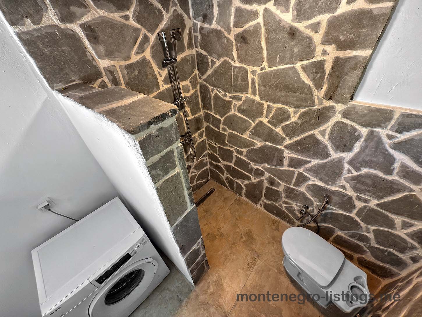 Modern bathroom in Ulcinj with stone tiles, open shower, washer, & toilet&mdash;ideal investment. Listed by Montenegro-listings.me (Ekosphere doo).