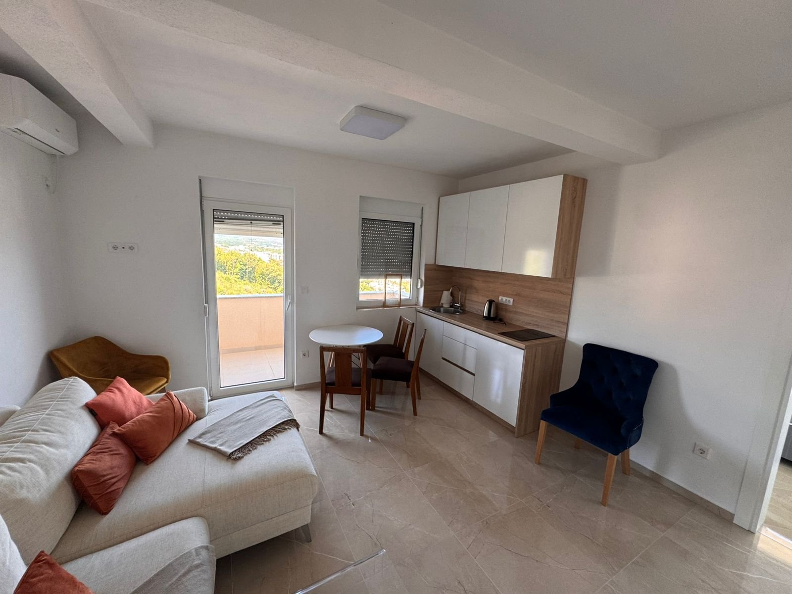 Modern Ulcinj apartment: white sofa, orange cushions, dining for two, balcony access. Top Montenegro investment at immorenta.me by Ekosphere doo.