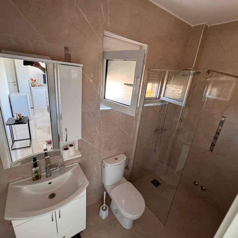 Contemporary Ulcinj bathroom: beige tiles, glass shower, window, and premium fixtures&mdash;ideal Montenegro real estate by ekosphere doo.