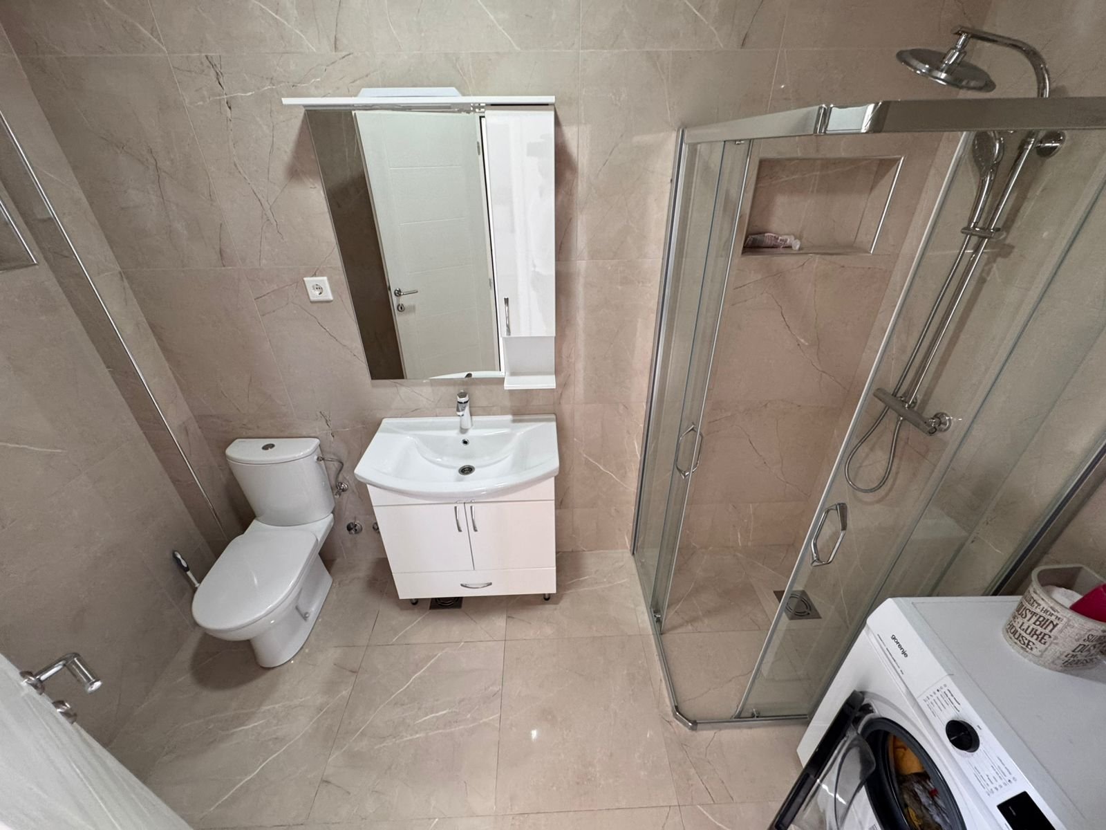 Contemporary bathroom in Ulcinj with beige tiles, glass shower, vanity, washer&mdash;ideal property investment listed at immorenta.me by ekosphere doo.