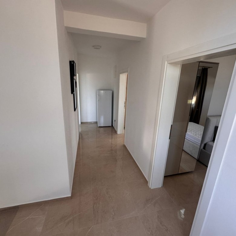 Bright hallway with beige tiles, white walls, and fridge leads to a bedroom&mdash;ideal Ulcinj investment. Listed by immorenta.me of ekosphere doo.
