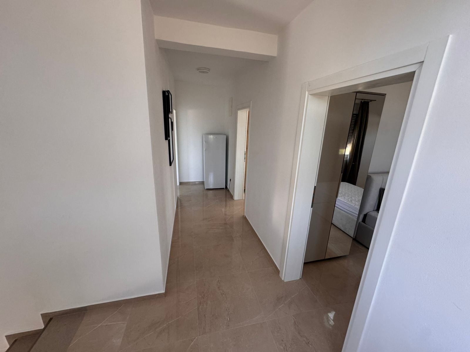 Bright hallway with beige tiles, white walls, and fridge leads to a bedroom&mdash;ideal Ulcinj investment. Listed by immorenta.me of ekosphere doo.