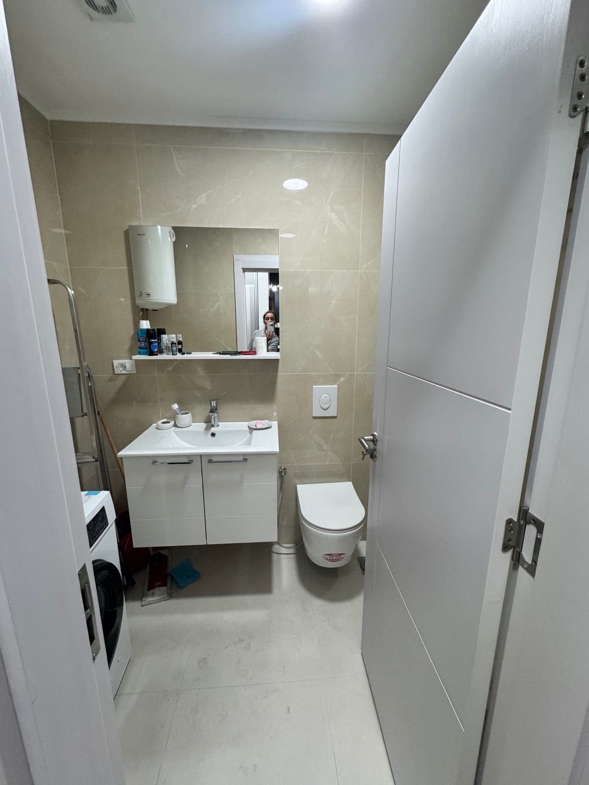 Modern Ulcinj bathroom with beige tiles, floating sink, wall-mounted toilet, washer; ideal real estate by ekosphere doo.