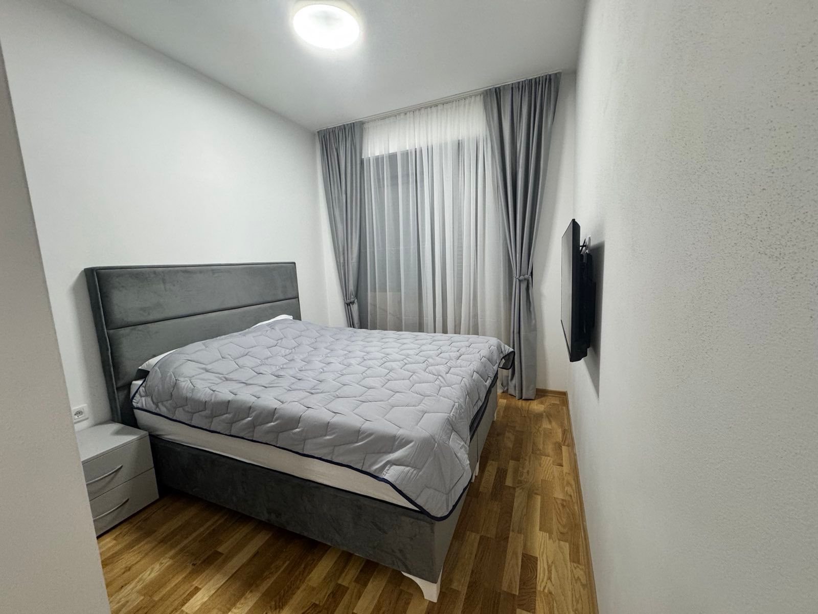 Elegant Ulcinj bedroom: spacious gray bed, wood floors, wall TV. Invest in Montenegro real estate at immorenta.me by ekosphere doo.