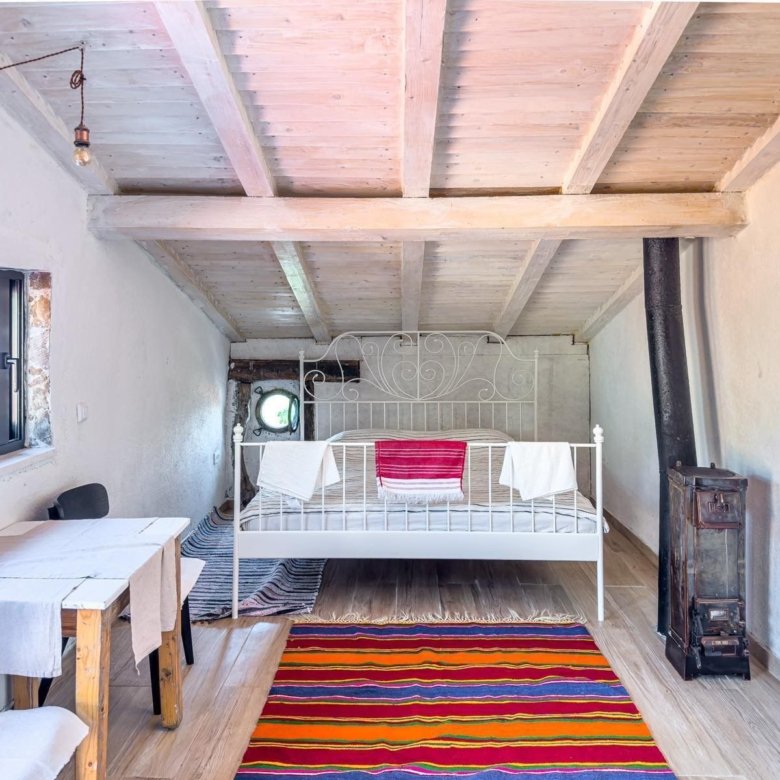 Stunning attic room in Ulcinj featuring a stylish bed, dining area, wood stove, and vibrant d&eacute;cor&mdash;exclusive on immorenta.me.