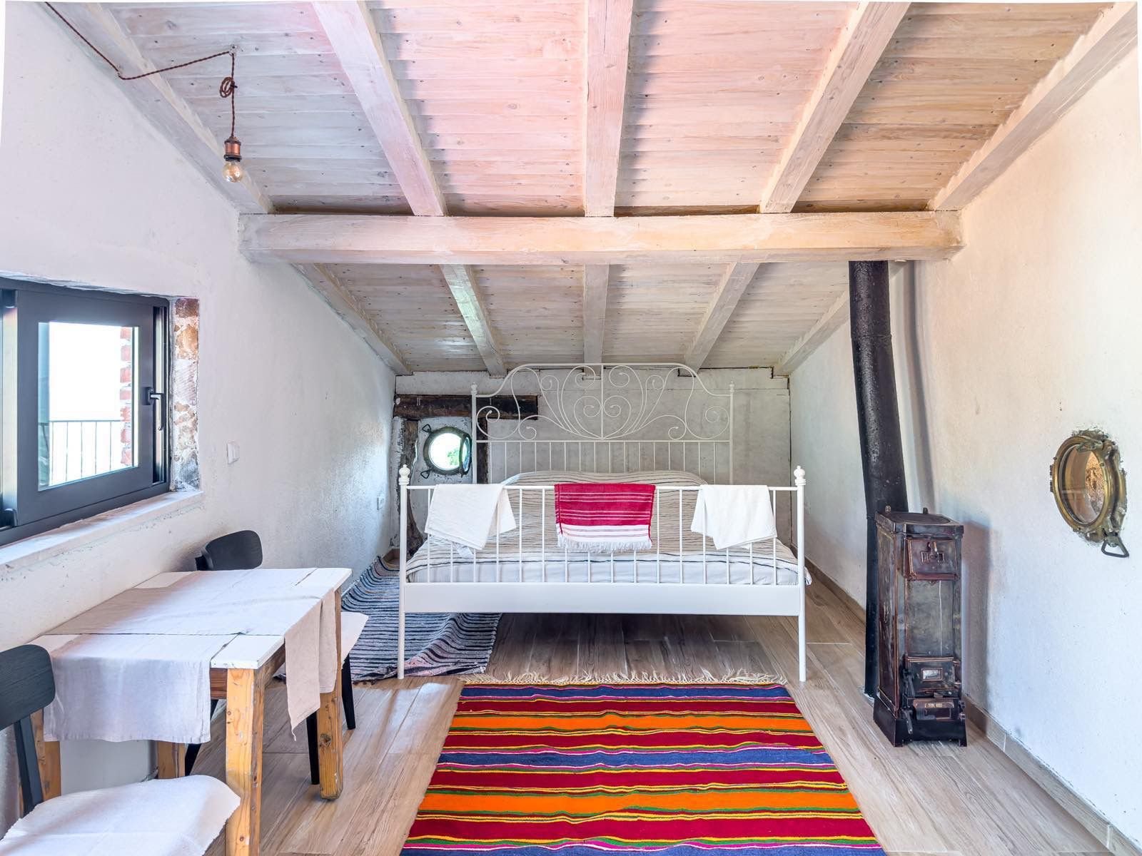 Stunning attic room in Ulcinj featuring a stylish bed, dining area, wood stove, and vibrant d&eacute;cor&mdash;exclusive on immorenta.me.