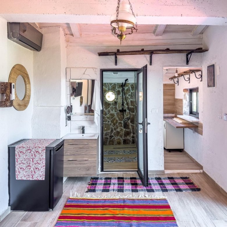 Modern Ulcinj apartment: bright, white walls, wood beams, stone-accent bath, custom sink, TV, colorful rugs. Exclusive to immorenta.me by ekosphere doo.