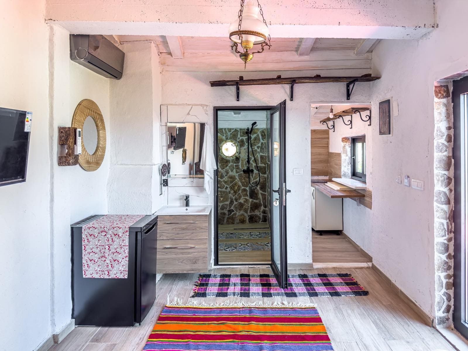 Modern Ulcinj apartment: bright, white walls, wood beams, stone-accent bath, custom sink, TV, colorful rugs. Exclusive to immorenta.me by ekosphere doo.