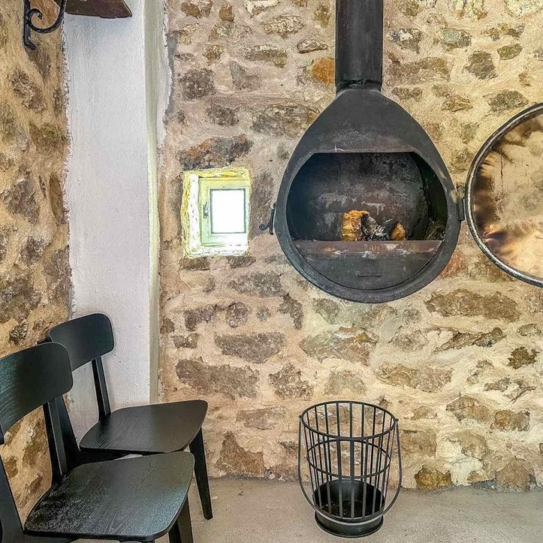 Charming stone-walled room in Ulcinj, Montenegro, featuring elegant black chairs, modern fireplace, and natural light&mdash;discover more on immorenta.me by ekosphere doo.