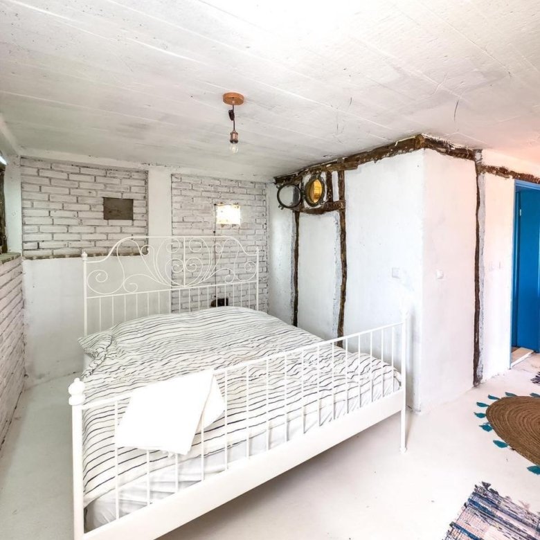 Modern Ulcinj bedroom with white walls, brick accents, stylish metal bed, blue door; ideal Montenegro investment via ekosphere doo.