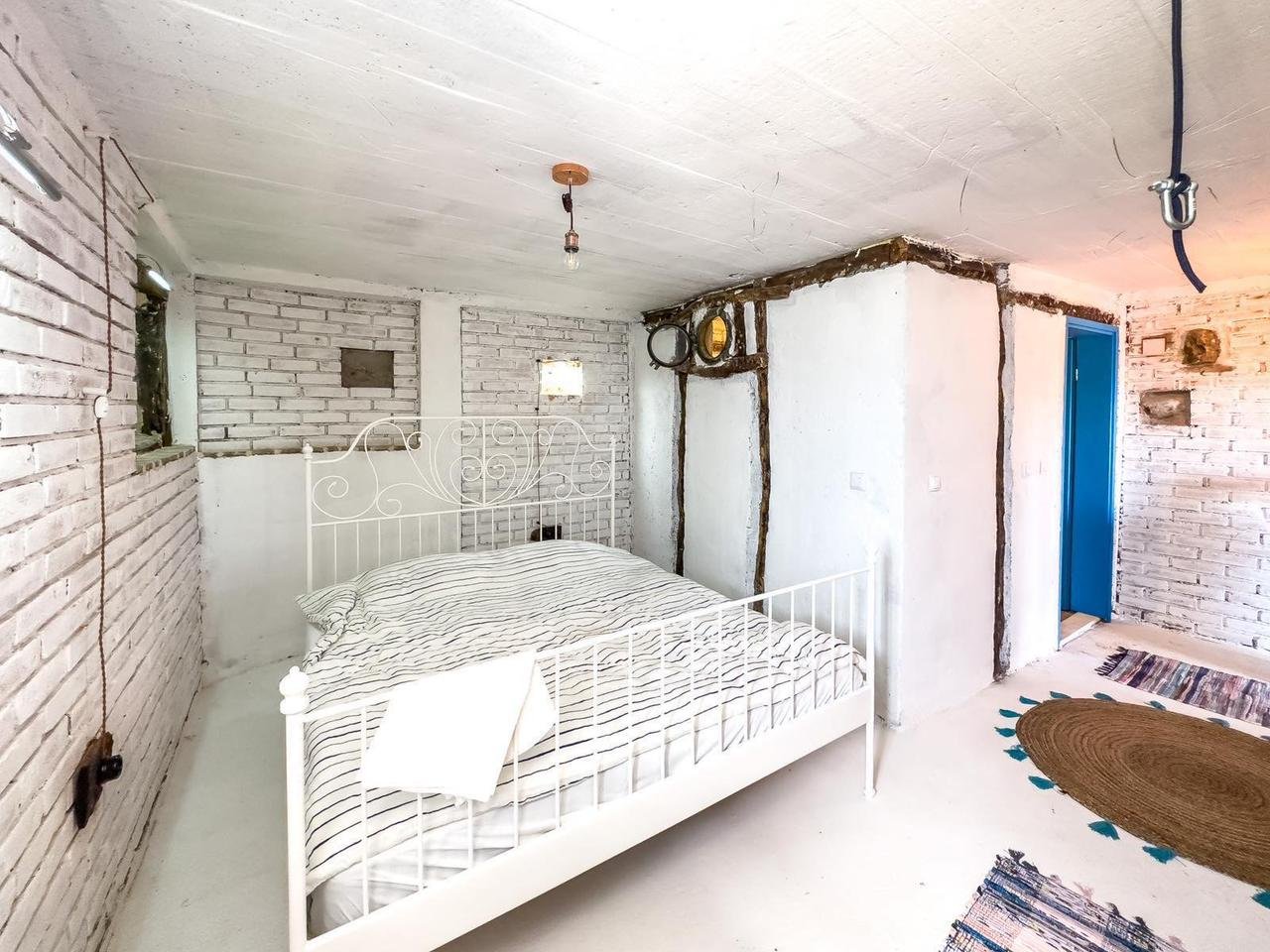 Modern Ulcinj bedroom with white walls, brick accents, stylish metal bed, blue door; ideal Montenegro investment via ekosphere doo.