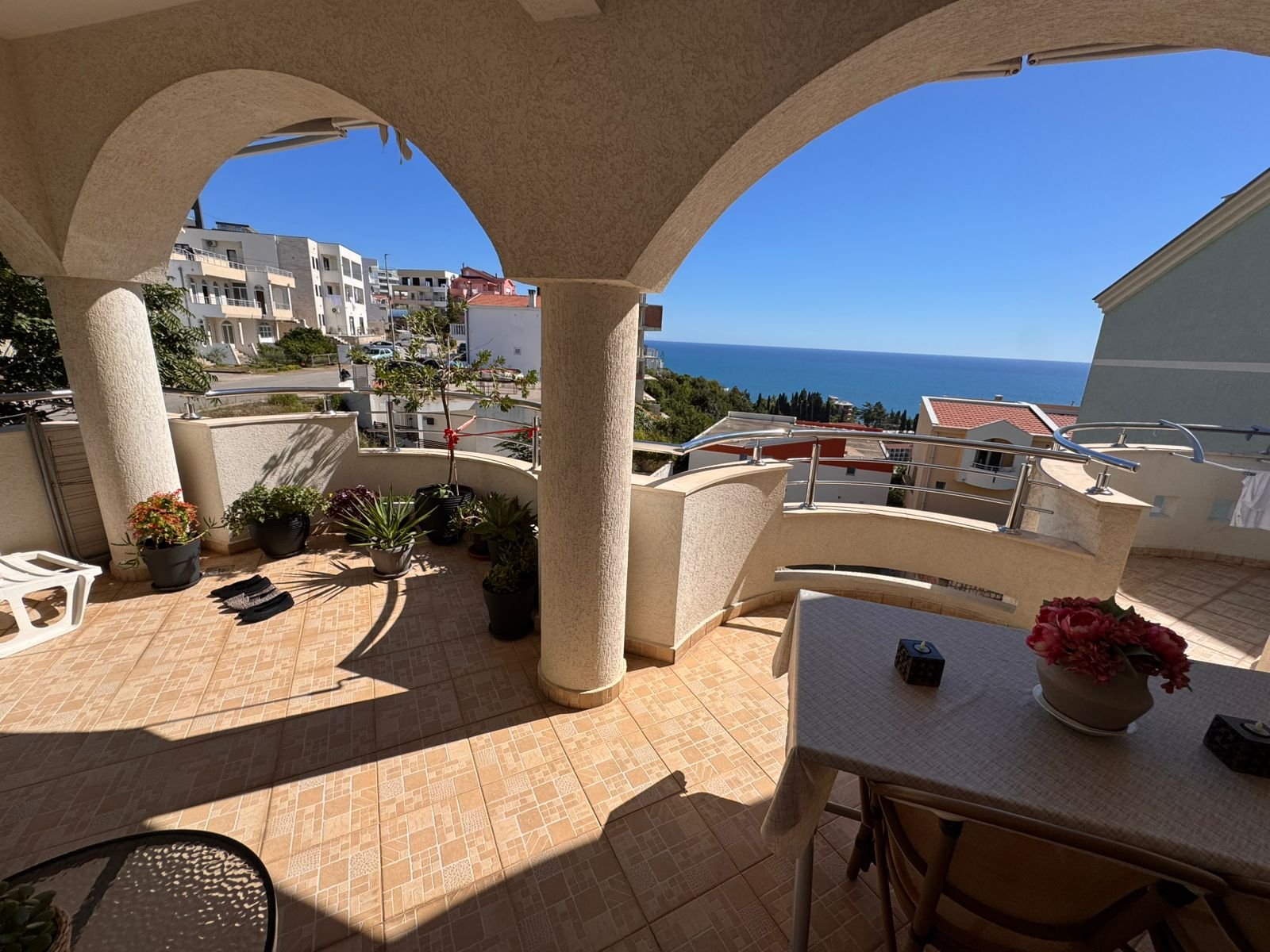 Spacious tiled balcony in Ulcinj with sea view, stylish columns, lush potted plants&mdash;exclusive property by immorenta.me.