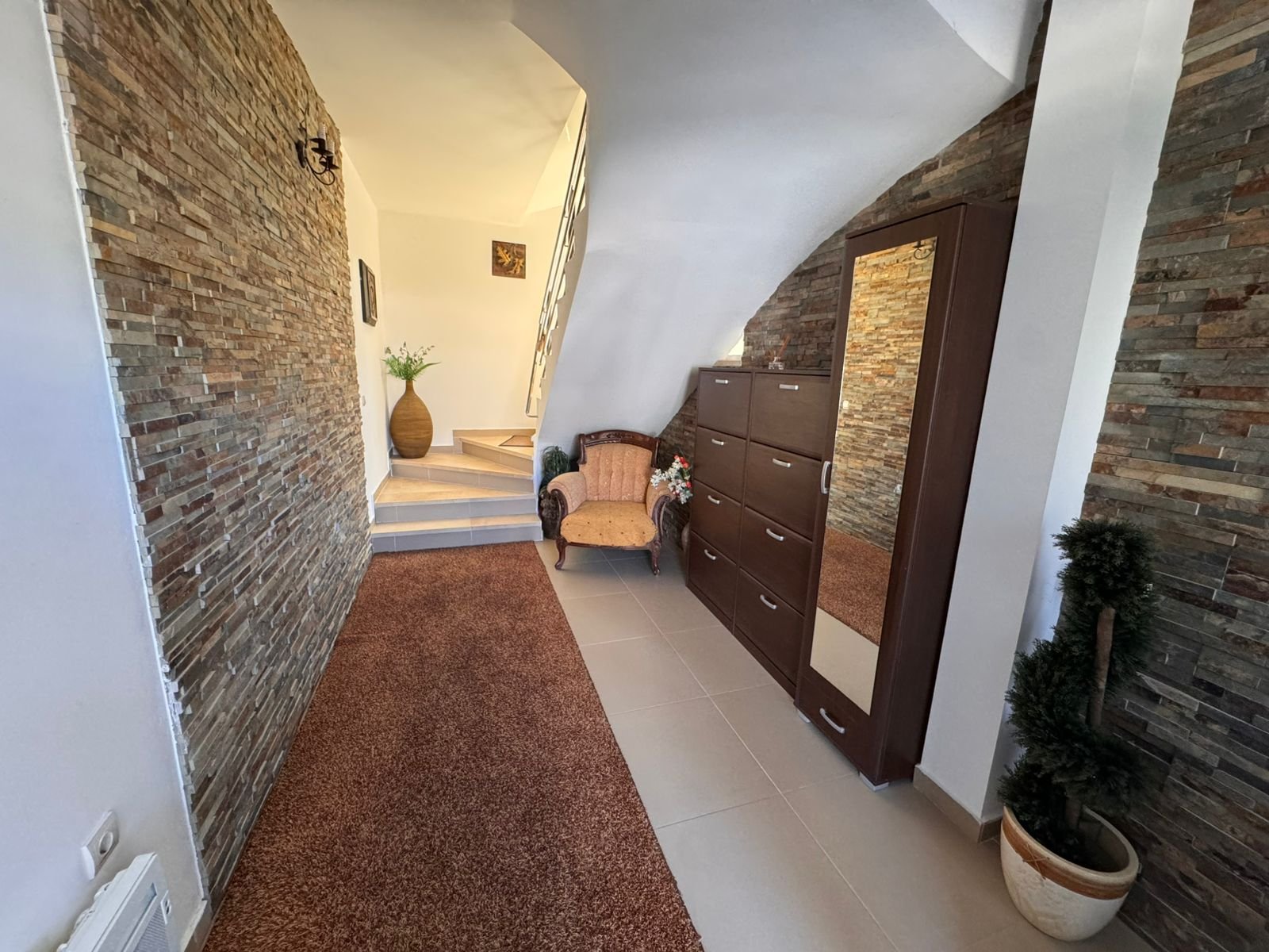 Elegant Ulcinj home with stone accents, plush chair, wood dresser, modern lighting; premium real estate on immorenta.me.