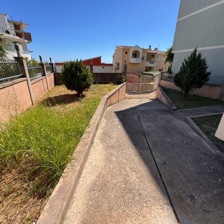 Inviting concrete driveway with lush grassy borders leads to secure gate, homes and apartments in scenic Ulcinj. Invest via Montenegro-Listings.me by ekosphere doo.