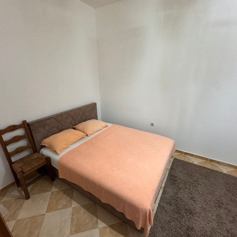 Modern Ulcinj bedroom with double bed, peach blanket, chair, tiled floor&mdash;ideal Montenegro investment. Exclusive on immorenta.me by ekosphere doo.