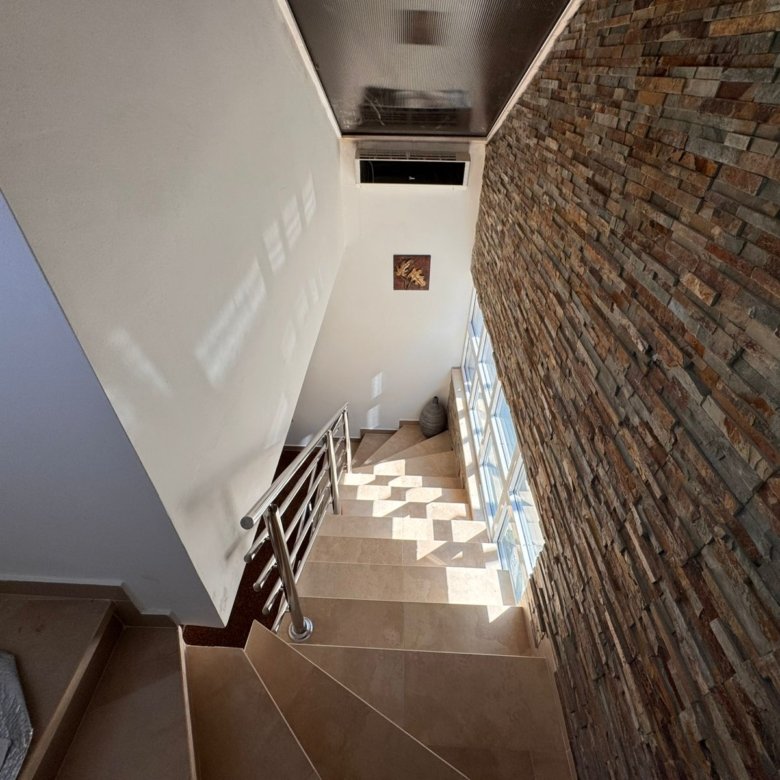 Elegant staircase with beige steps, metal railing, stone accents, and large windows&mdash;prime Ulcinj real estate on immorenta.me.
