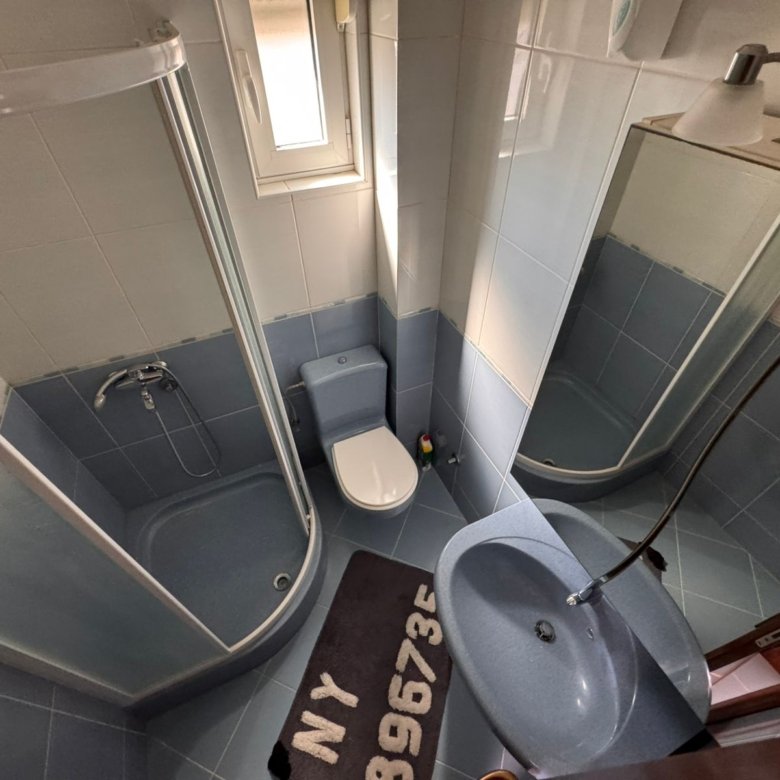 Modern bathroom in Ulcinj with blue tiles, glass shower, curved sink, and large mirror&mdash;exclusive real estate by ekosphere doo.