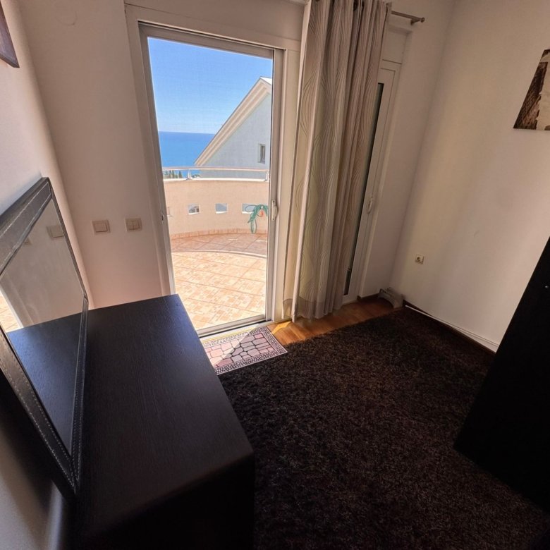 Modern Ulcinj apartment: stylish room with dark furnishings, sea-view balcony, glass door, and curated art. Exclusive on immorenta.me by ekosphere doo.