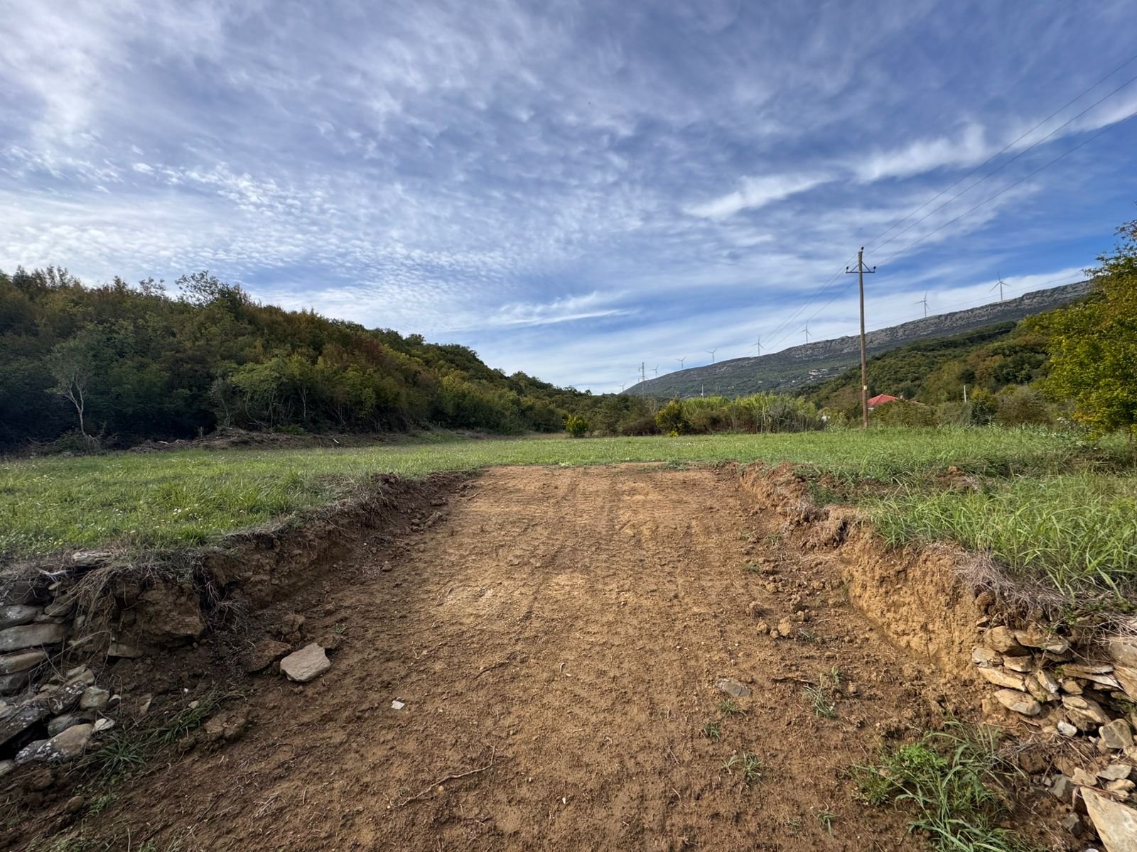 Scenic Ulcinj land with lush greenery, hills, and wind turbines&mdash;prime real estate investment via immorenta.me by ekosphere doo.