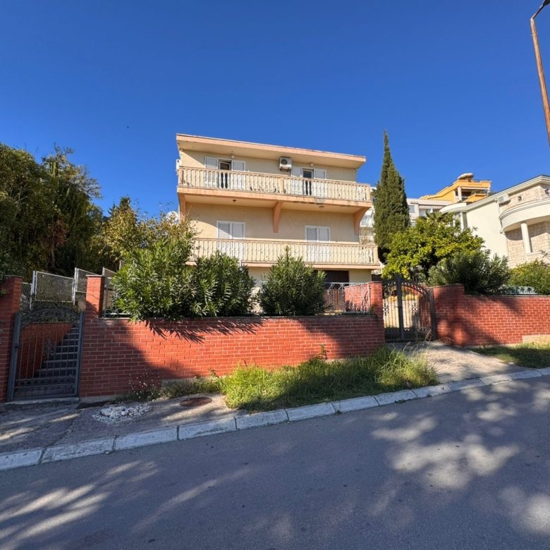 Stunning three-story yellow home with balconies, brick fence, and lush greenery in Ulcinj. Exclusive at immorenta.me by ekosphere doo.