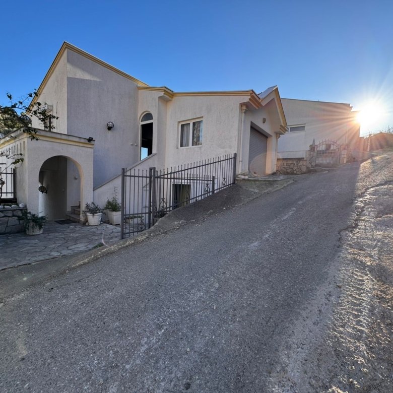 Elegant two-story white house in Ulcinj, Montenegro with arched entryway, metal gate, and hill views&mdash;exclusive at immorenta.me.