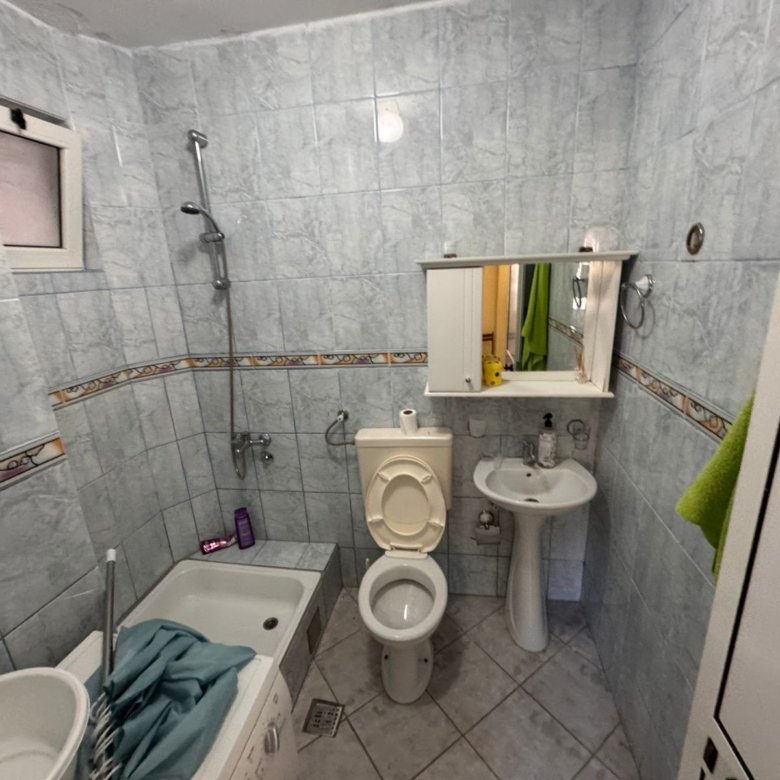 Modern tiled bathroom in Ulcinj features bathtub, handheld shower, wall-mounted sink, and storage&mdash;ideal Montenegro real estate investment.