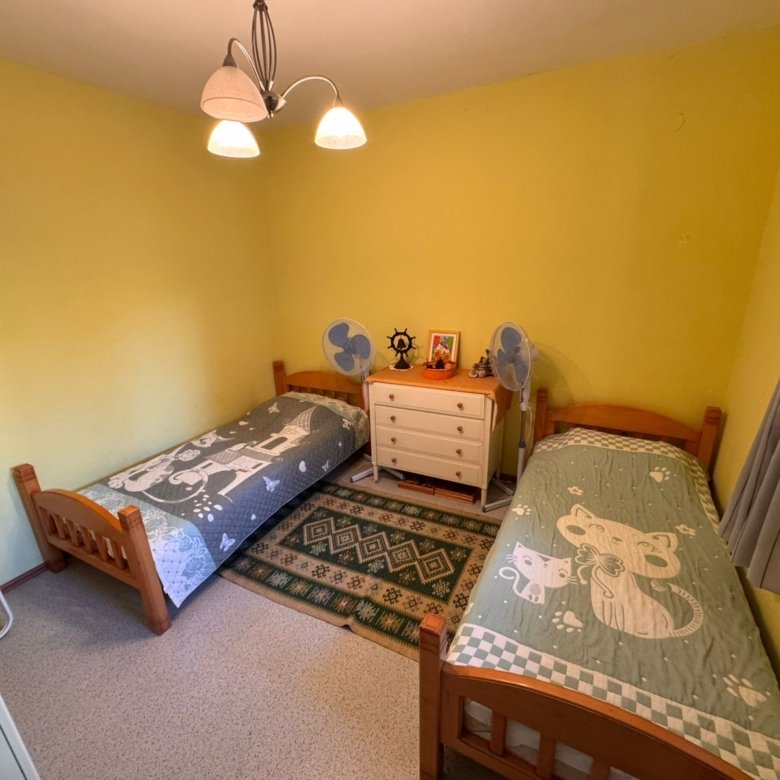 Cozy Ulcinj bedroom with vibrant yellow walls, twin wooden beds, green rug, and ample storage&mdash;a great Montenegro investment.