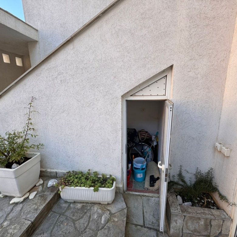 Spacious white storage unit under stairs, ideal for Ulcinj Montenegro property investors. Includes organized tools, garden access, and entry plants. Montenegro-listings.me by ekosphere doo.