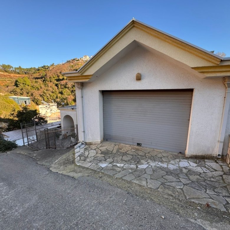 Modern white garage with secure gray door on a sloped lot, stone-paved drive, scenic Ulcinj views&mdash;exclusive at immorenta.me.