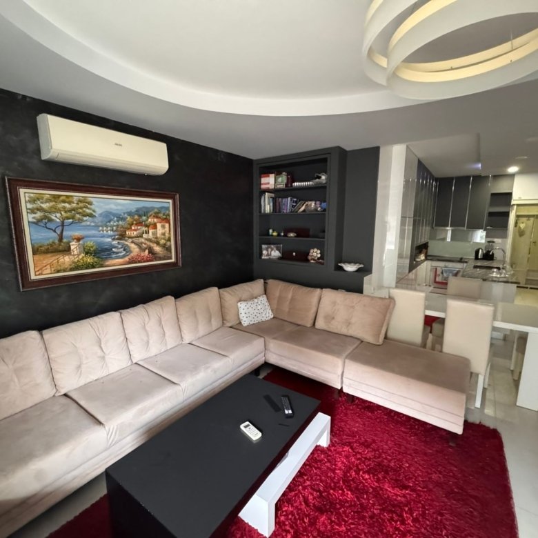 Stylish Ulcinj apartment: modern living room, beige L-sofa, red rug, open kitchen/dining. Prime Montenegro investment&mdash;ekosphere doo.
