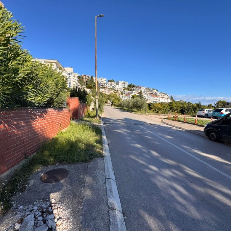 Prime Ulcinj property on a scenic uphill road with lush greenery, brick wall, and city views. Listed by ekosphere doo, Montenegro.