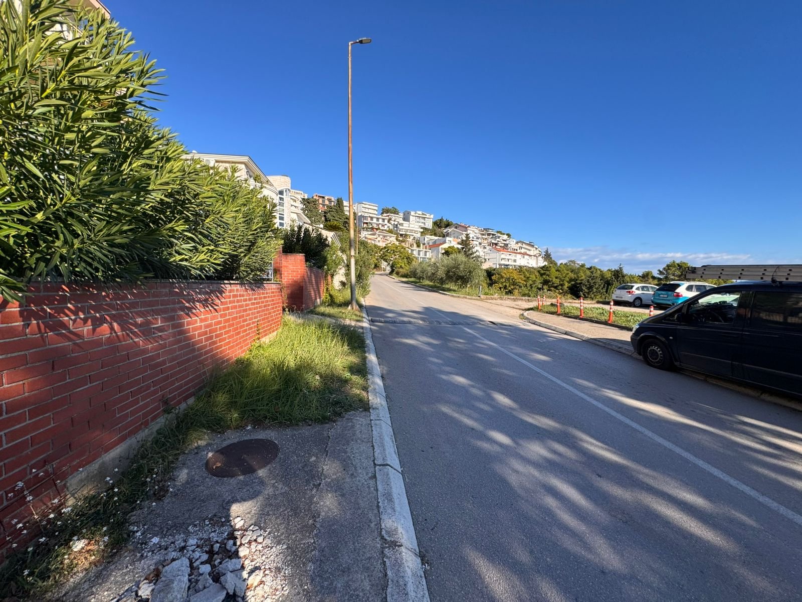 Prime Ulcinj property on a scenic uphill road with lush greenery, brick wall, and city views. Listed by ekosphere doo, Montenegro.