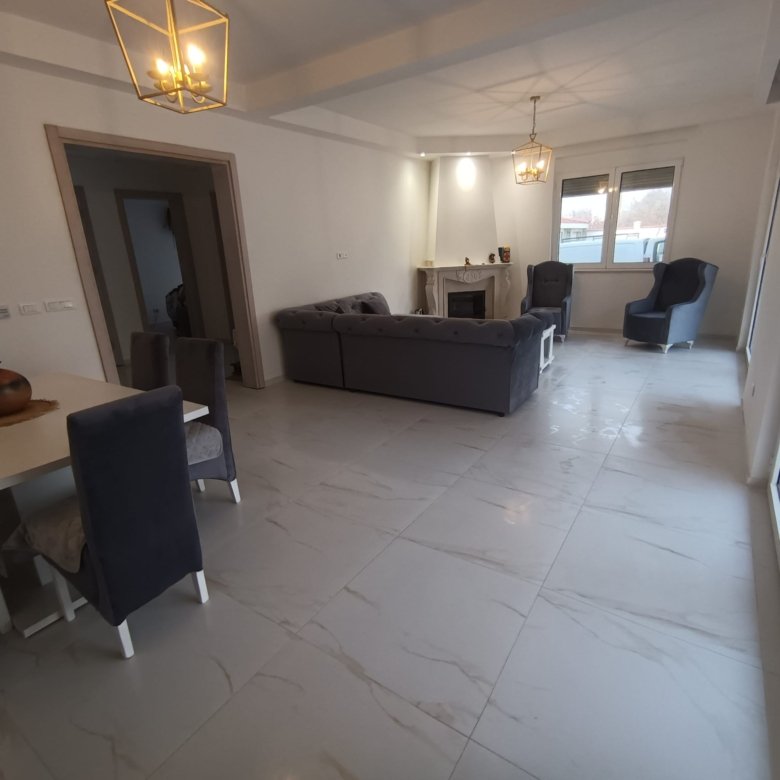 Modern Ulcinj living room with light tile flooring, designer gray sofas, fireplace, dining area, large windows&mdash;ideal investment. Montenegro-listings.me by ekosphere doo.