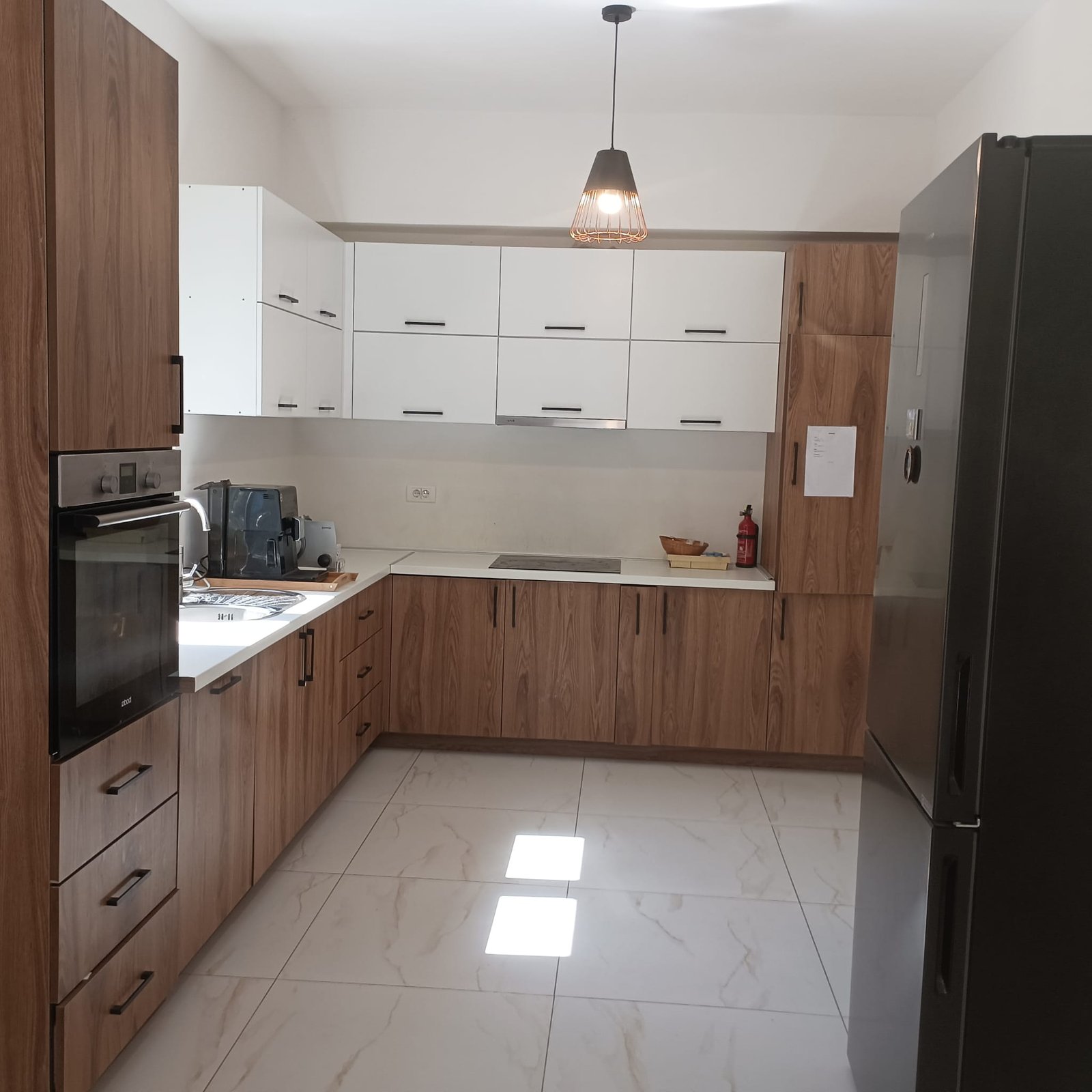 Contemporary Ulcinj kitchen: wood/white cabinetry, built-in oven, stainless fridge, sunlit tile floor. Montenegro-listings.me by ekosphere doo.