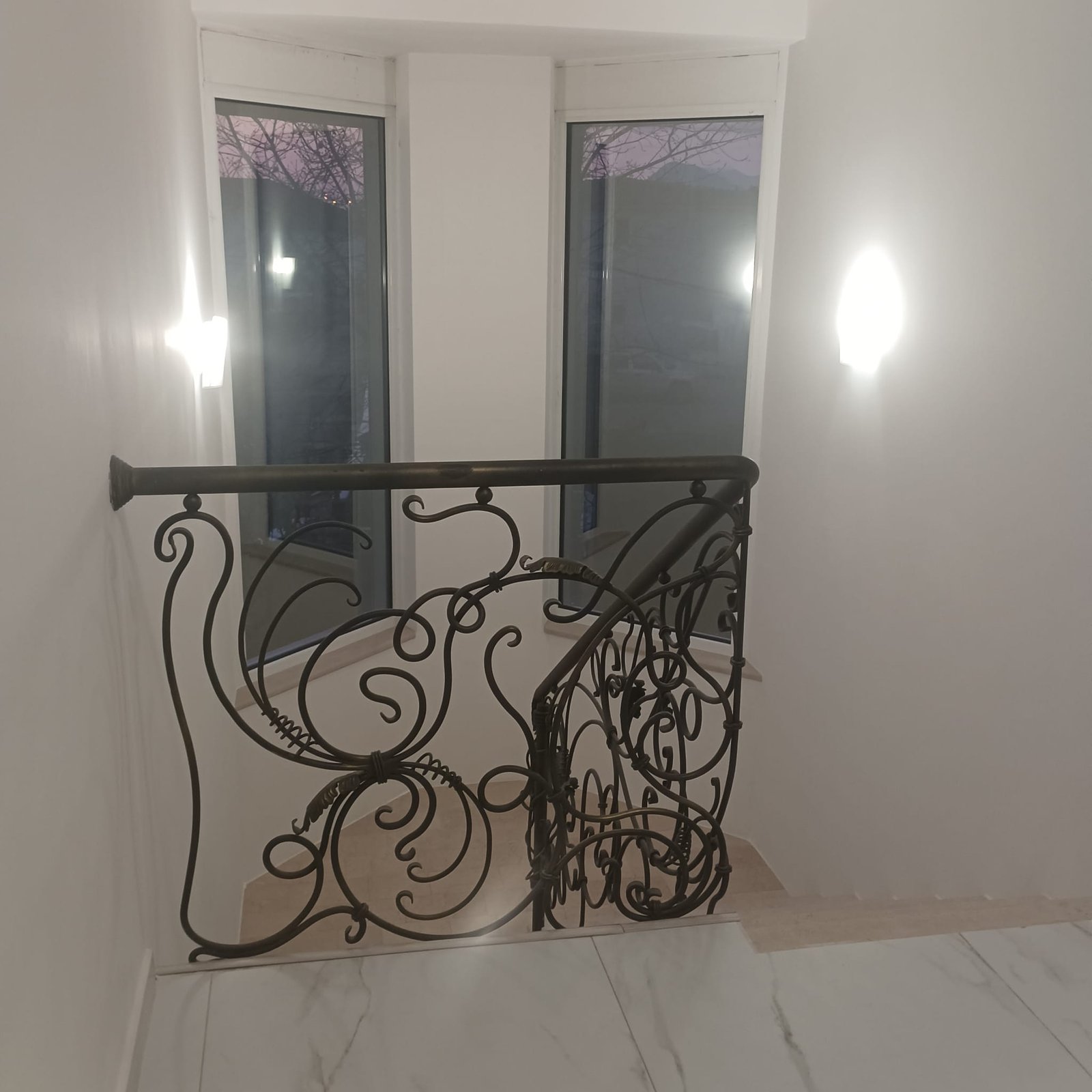 Elegant staircase with ornate metal railing, modern lighting, and floor-to-ceiling windows&mdash;prime Ulcinj property on immorenta.me by ekosphere doo.