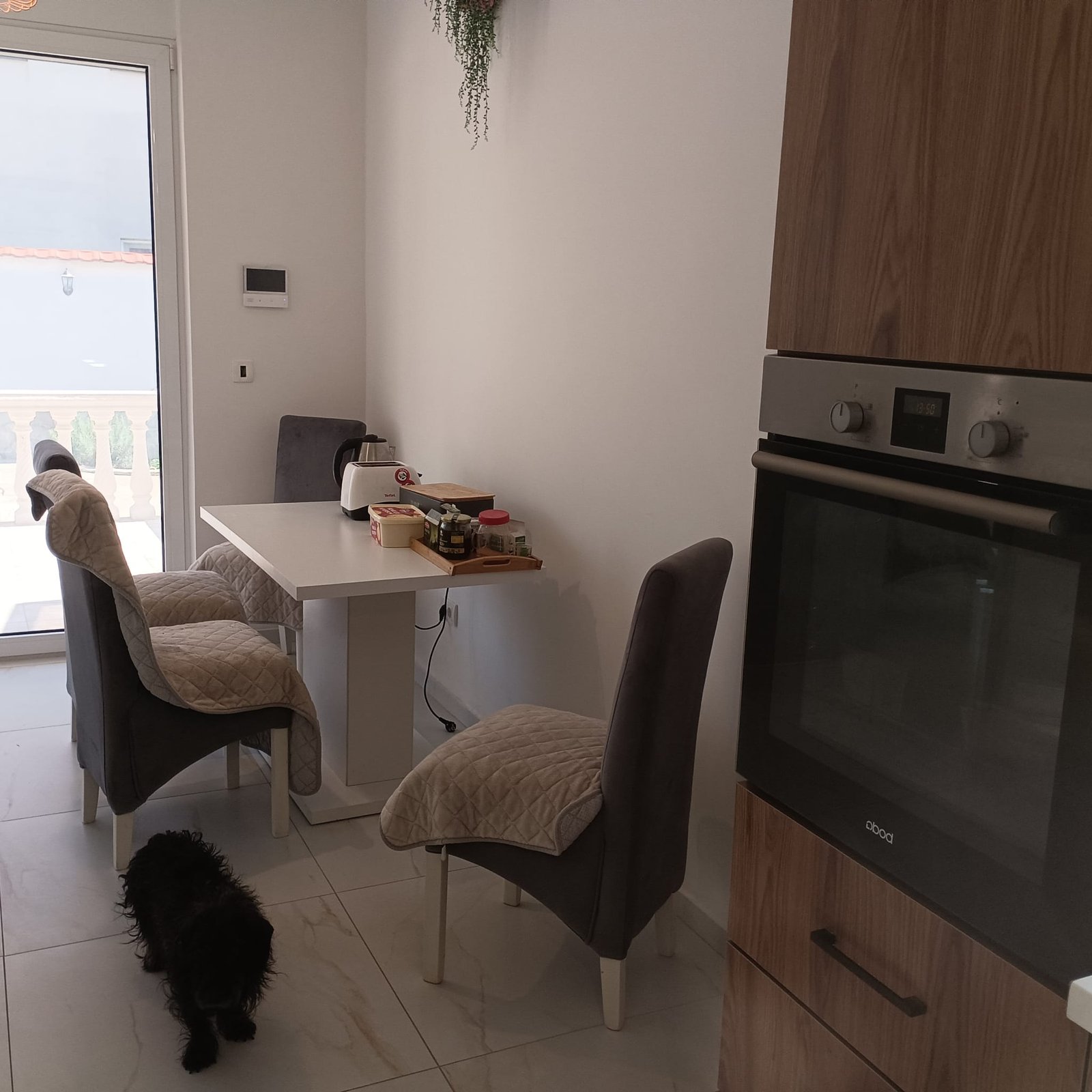 Modern dining area in Ulcinj features a white table, gray chairs, wall oven, balcony access; ideal Montenegro investment by ekosphere doo.