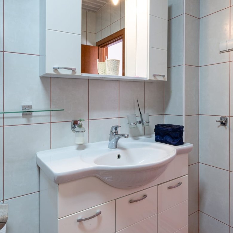 Modern Ulcinj bathroom: white tiles, sleek sink cabinet, illuminated mirror. Perfect for property investment at immorenta.me.