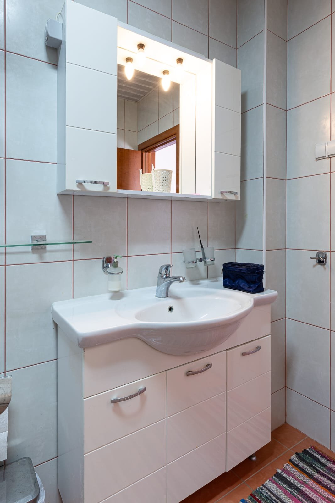 Modern Ulcinj bathroom: white tiles, sleek sink cabinet, illuminated mirror. Perfect for property investment at immorenta.me.