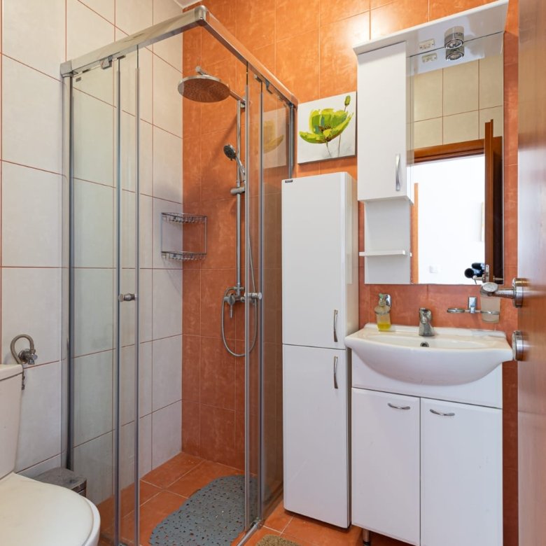 Modern Ulcinj bathroom with stylish orange-white tiles, glass shower, premium fixtures. Exclusive on immorenta.me by ekosphere doo.